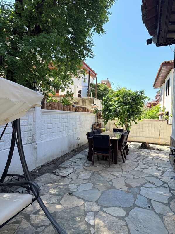 An outdoor patio with stone flooring, a table with chairs, and a white wall with a textured pattern.