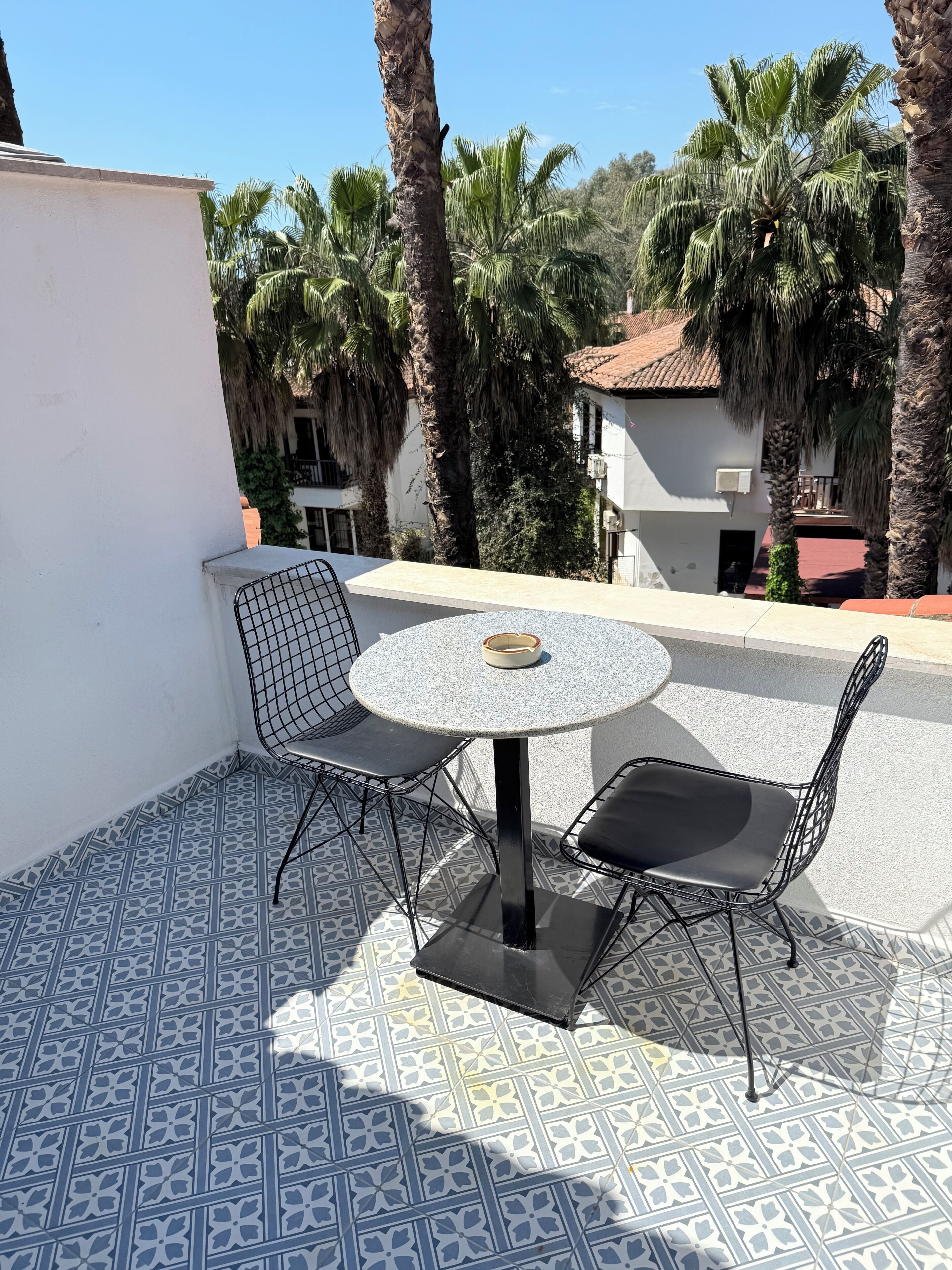 A terrace with a round table and two chairs, surrounded by patterned tiles.