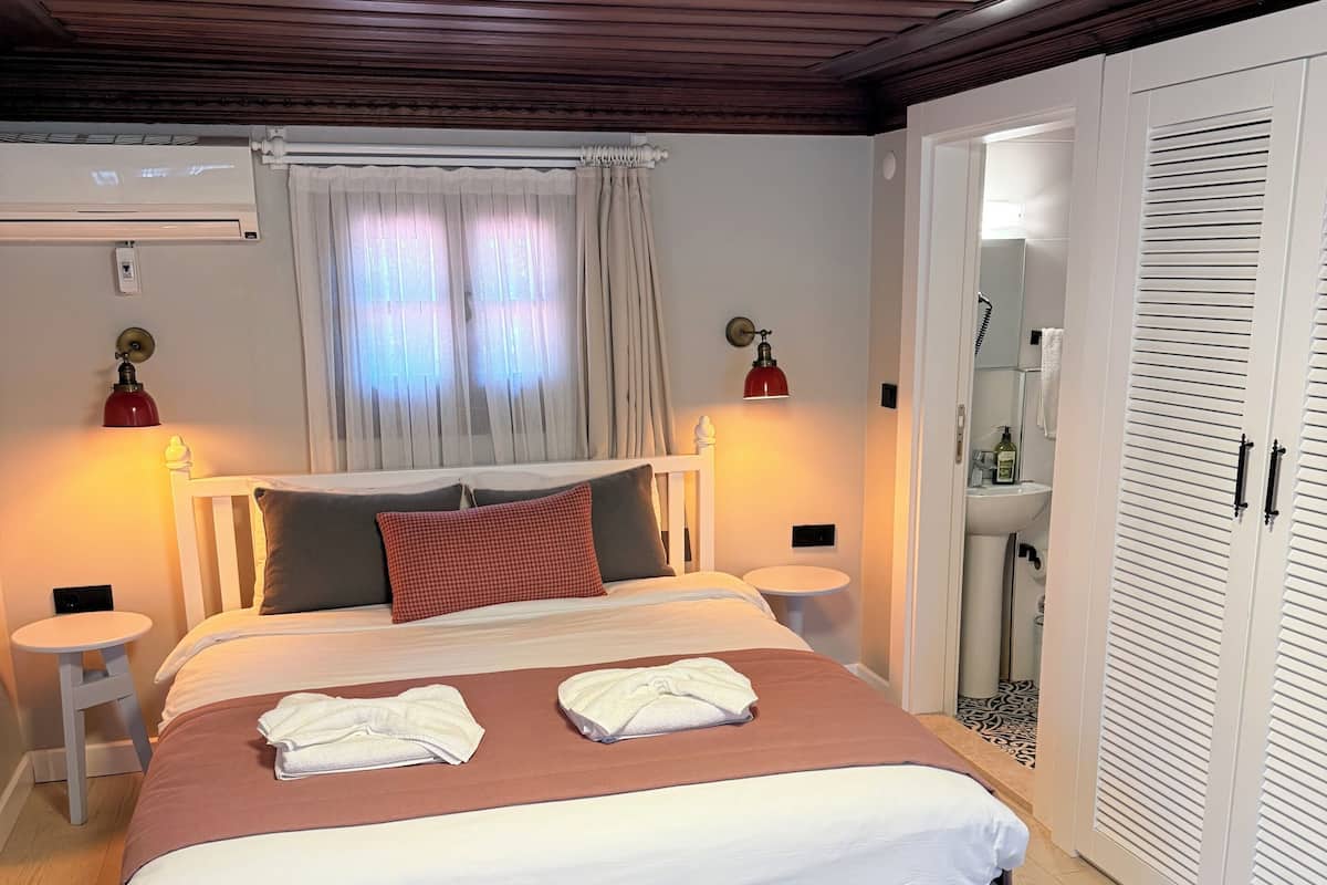 Une chambre à coucher bien rangée, avec un lit, des tables de chevet, une armoire et une salle de bain visible à travers une porte ouverte.