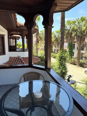 Un espace extĂ©rieur amĂ©nagĂ©, abritĂ© et dotĂ© dâune table en verre et de chaises en osier, offrant une vue sur une cour intĂ©rieure avec des palmiers et un scooter garĂ©.