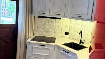 Una cocina compacta con armarios blancos, un lavamanos negro y un salpicadero con estampado de espiga.