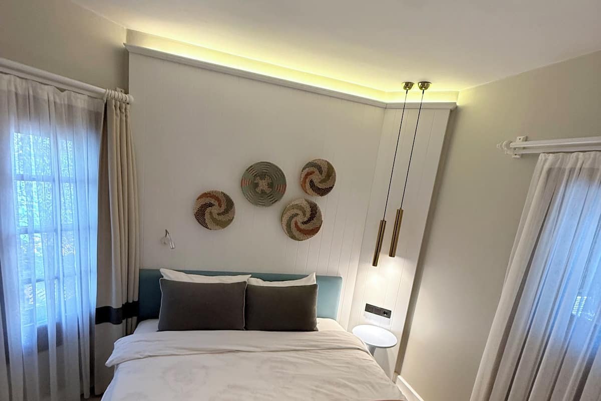 Une chambre d’hôtel avec un lit, des rideaux, un élément de décoration circulaire au mur, une table de chevet et une lampe.