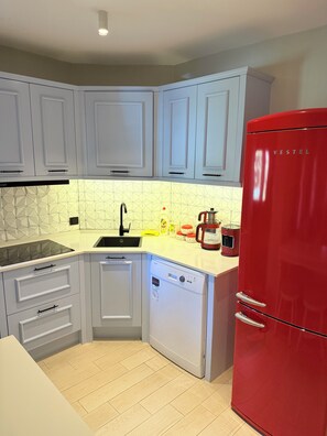 Una cocina compacta con armarios blancos, un refrigerador rojo, lavavajillas y un lavadero con un protector contra salpicaduras de diseño geométrico.