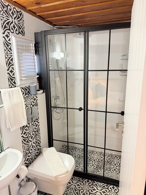 A bathroom with a shower, toilet, and sink, featuring patterned tiles and a wooden ceiling. - Jasmine Suıts (ula)