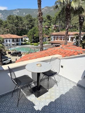 A patio with a round table and two chairs, a swimming pool, and buildings with red-tiled roofs. - Jasmine Suıts (ula)