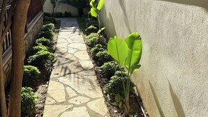A stone pathway flanked by lush greenery and a wall. - Jasmine Suıts (ula)