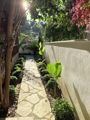 A stone pathway flanked by lush greenery and a wall. - Jasmine Suıts (ula)