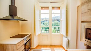 A kitchen with a stove, oven, and a view of a green landscape through a door. - LITTLE PALACE MIRADOR The best panoramic views (Besalu)