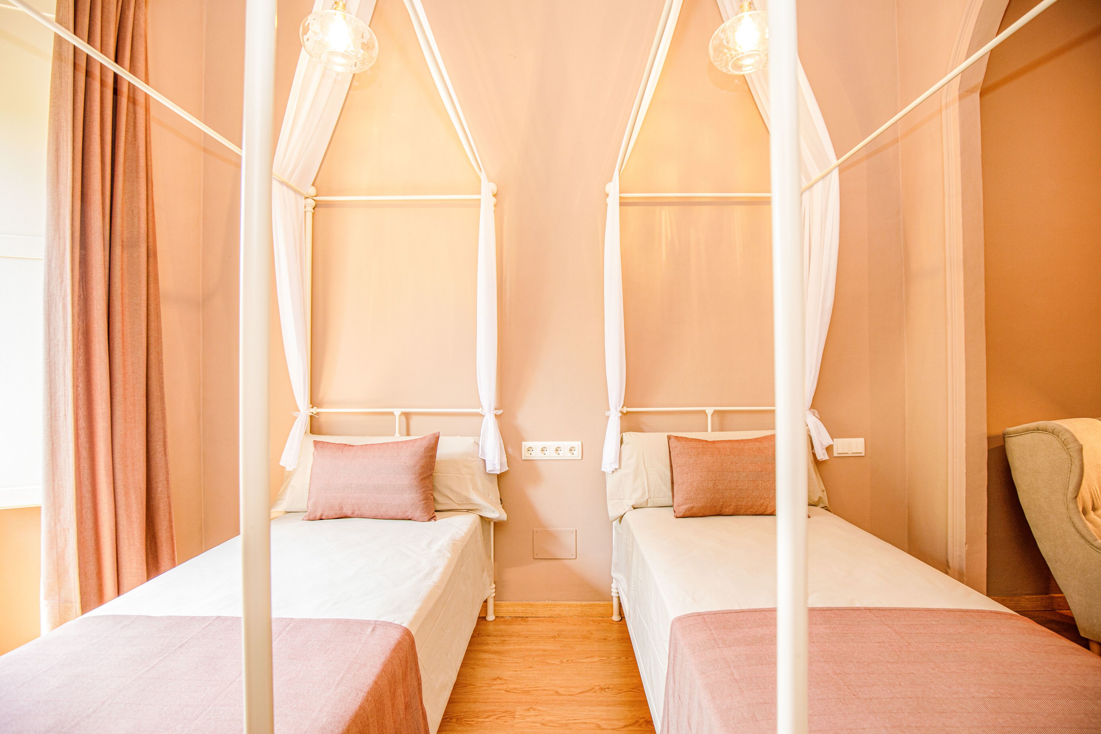 Ein Zimmer mit zwei Betten, jedes mit Baldachin, einem Sessel und Holzboden.