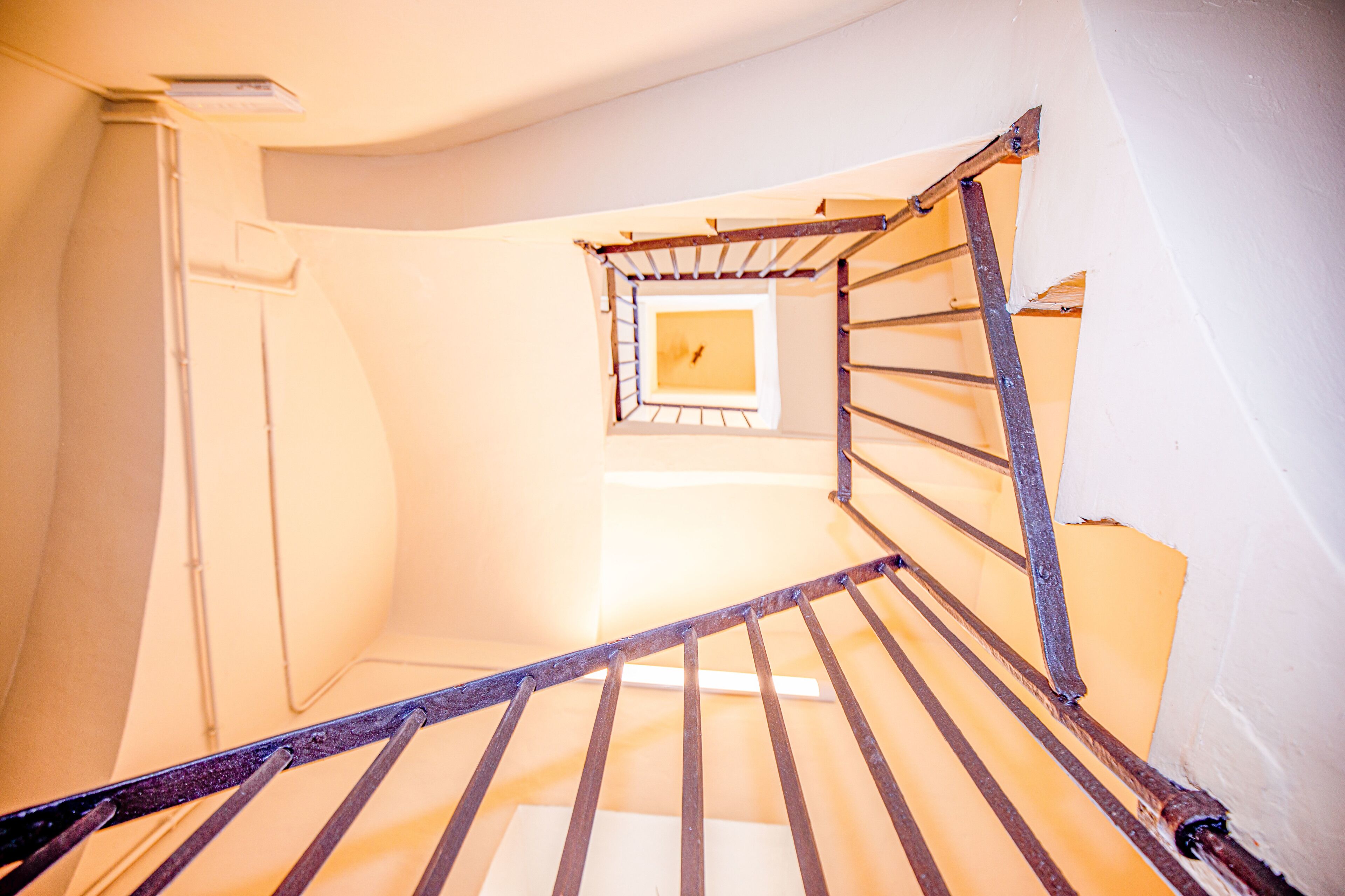 A spiral staircase with a metal railing, a small window at the top, and a white wall.