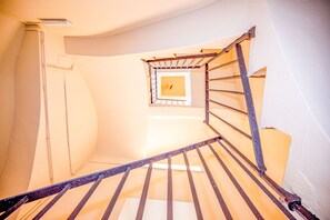 Eine Wendeltreppe mit Metallgeländer, ein kleines Fenster oben und eine weiße Wand.