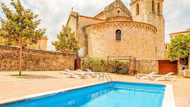 A swimming pool with lounge chairs, a stone building with a bell tower, and a clear sky. - LITTLE PALACE SWIMING POOL Unique in the center (Besalu)