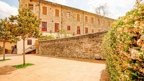 A stone building with multiple windows and doors, a paved courtyard, and a tree. - LITTLE PALACE SWIMING POOL Unique in the center (Besalu)