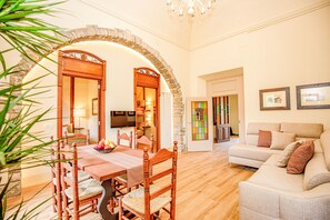 Un comedor con una mesa y sillas de madera, un arco de piedra, una sala de estar con sofá y televisor.