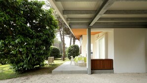 Um espaço ao ar livre coberto, com um caminho de pedrisco, um banco de madeira e uma pequena mesa com cadeiras.