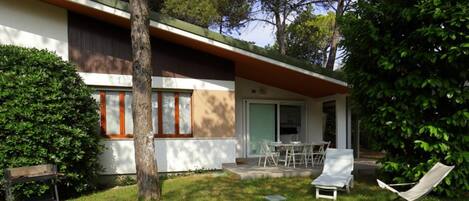 A modern house with a covered patio, a lawn, and a tree.