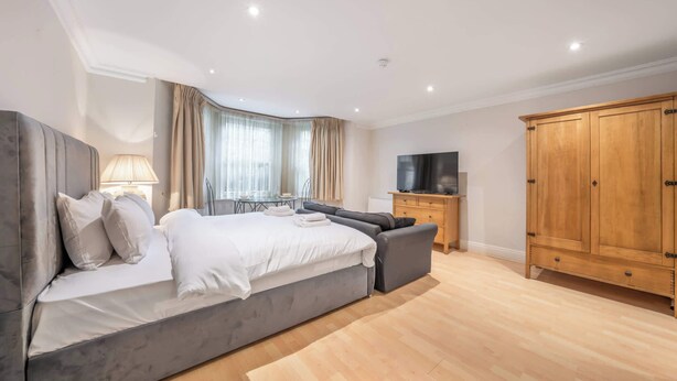 A bedroom with a large bed, a TV, a wardrobe, and a desk with a lamp. - Comfort Studio Apartment in Knightsbridge (Greater London)