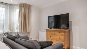 A modern living room with a sofa, a wooden TV stand, and a radiator. - Comfort Studio Apartment in Knightsbridge (Greater London)