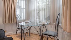 A round glass table with metal chairs, a window with sheer curtains, and a staircase in the background. - Comfort Studio Apartment in Knightsbridge (Greater London)