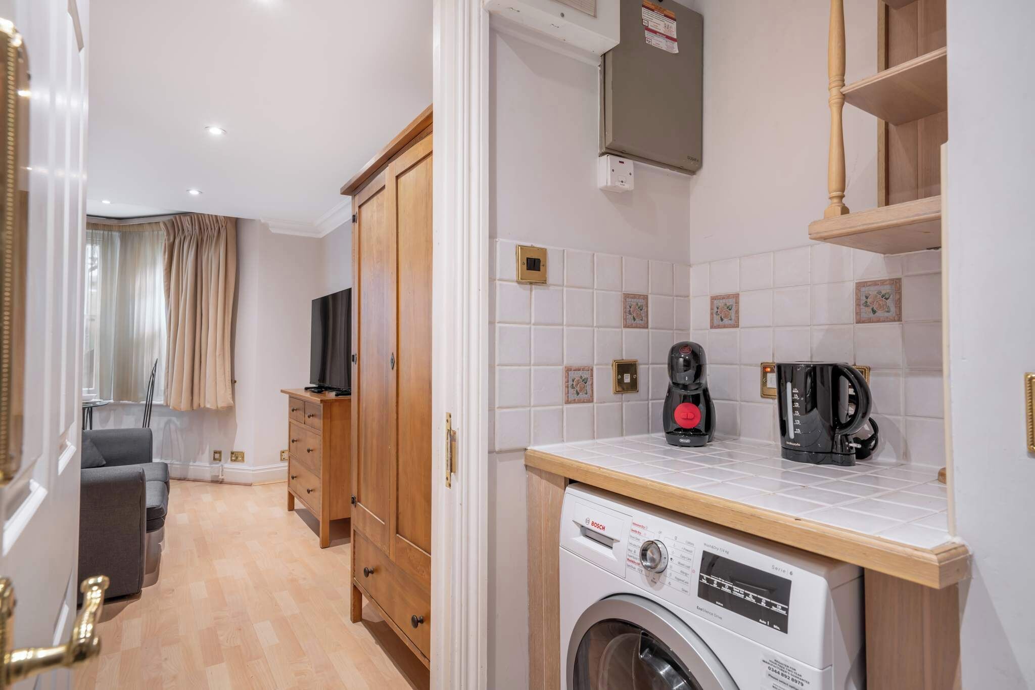 Une cuisine compacte équipée d’un lave-linge, d’une machine à café et d’un téléviseur.