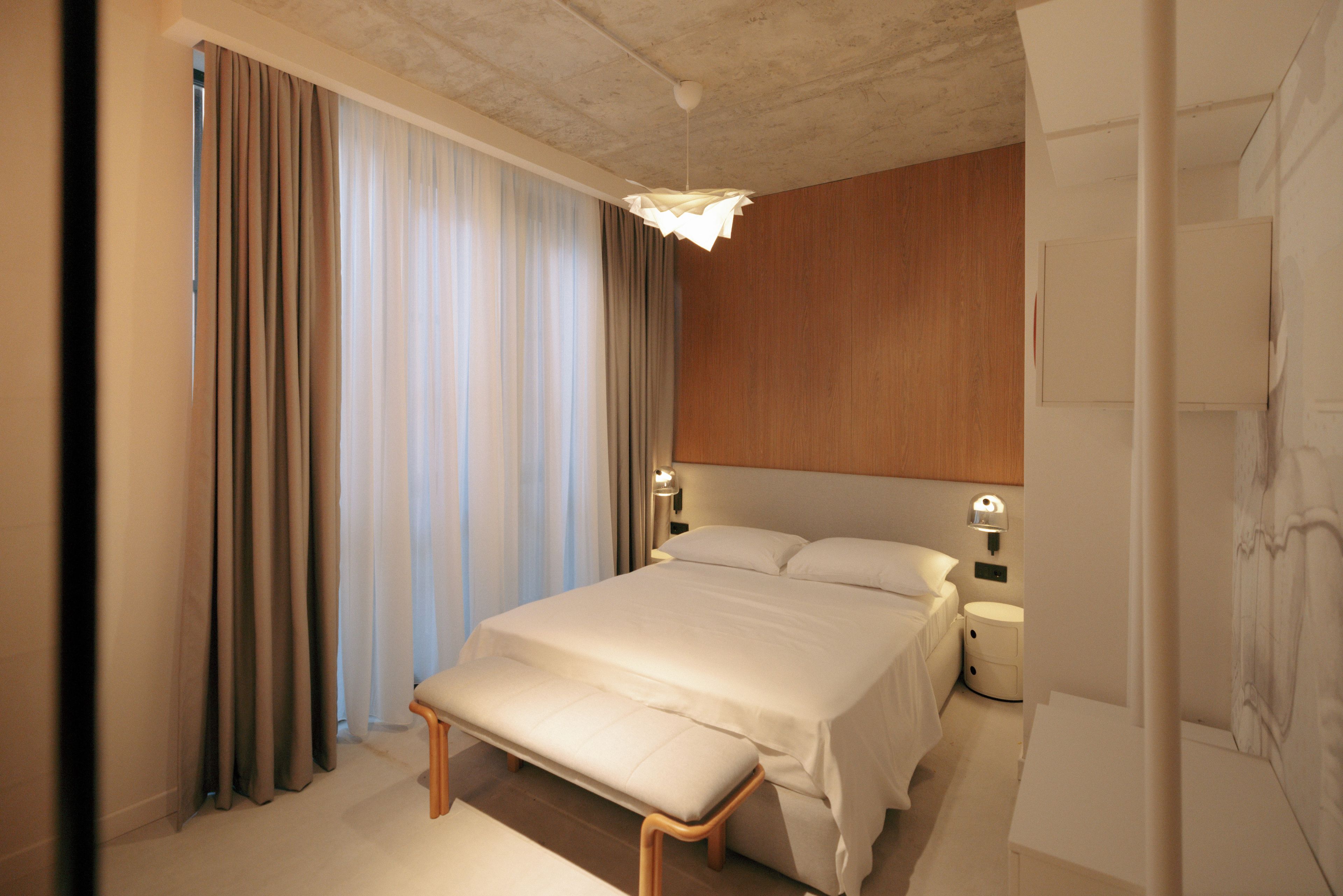 A hotel room with a large bed, bedside tables, a bench, and curtains.