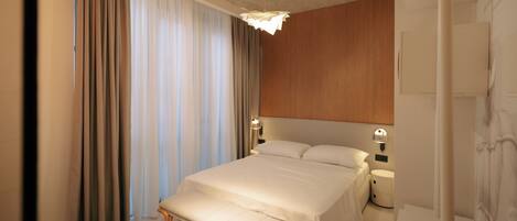 A hotel room with a large bed, bedside tables, a bench, and curtains.