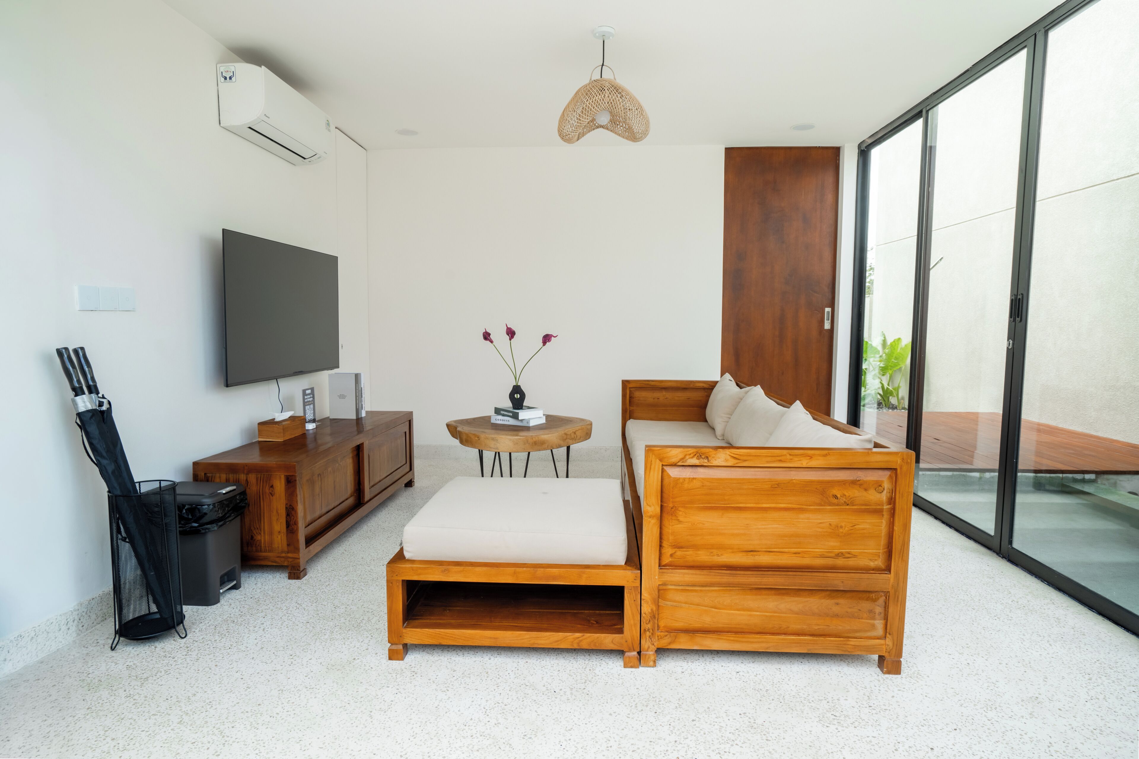 A modern living room with a sofa, a TV, a small table with books, and a wicker lamp.