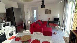 Eine moderne Küche mit Waschmaschine, ein Essbereich mit Tisch für Zwei, ein rotes Sofa und ein Fernseher im Wohnbereich.