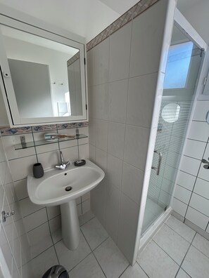 A bathroom with a white sink, mirror, and glass shower enclosure. - La Providence (La Tremblade)