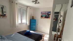 Ein Schlafzimmer mit Bett, blauem Schminktisch, einem Fenster mit Jalousien, Deckenventilator und Spiegel.