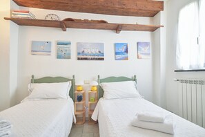 A room with two beds, a wooden shelf with books, a clock, and seascape paintings on the wall. - La Dimora Blu (Albenga)