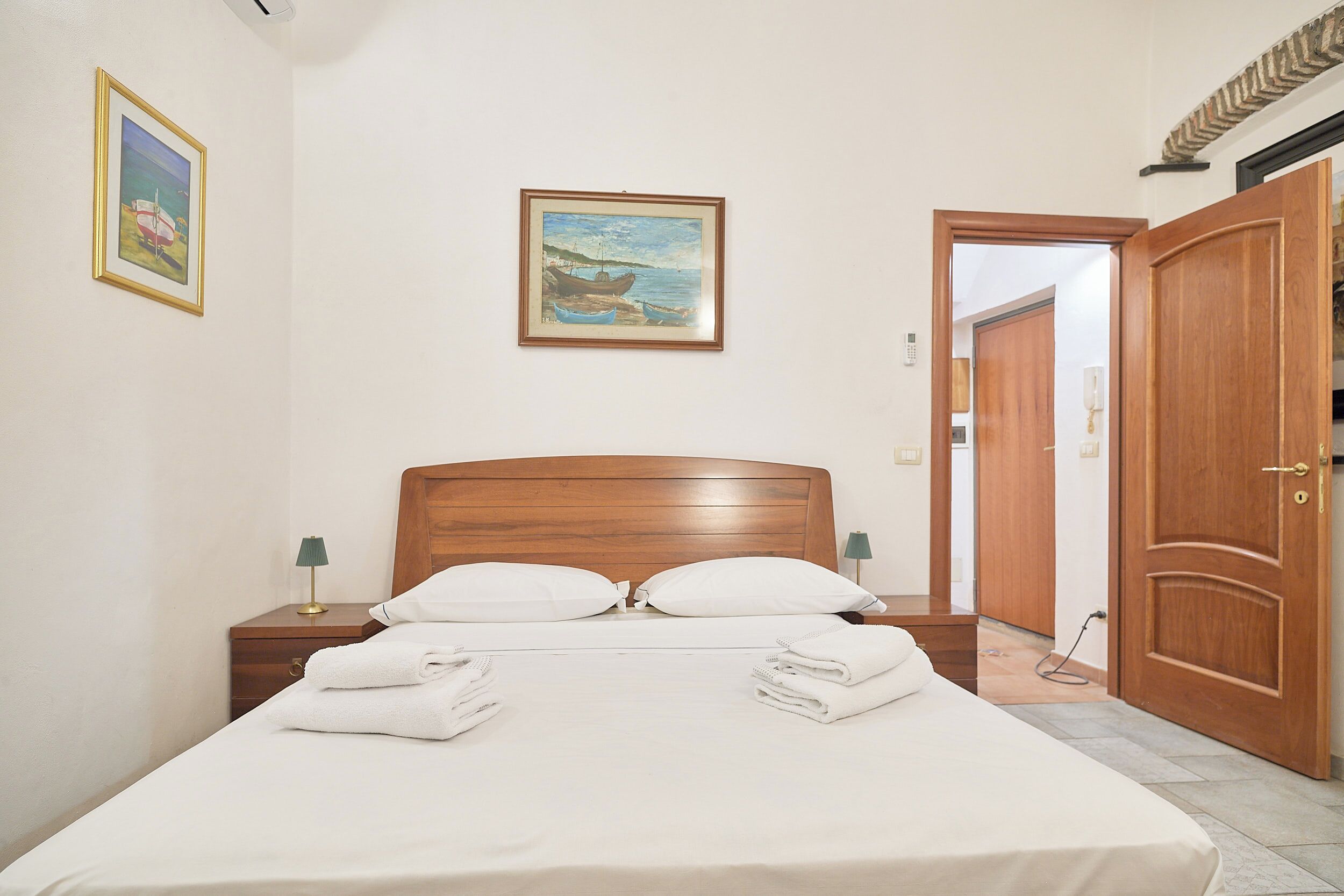 A neatly made bed with white linens, a wooden headboard, and two bedside lamps.