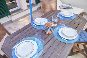 A wooden table set with blue placemats, white plates, and clear glasses. A teddy bear is placed on the table. - La Dimora Blu (Albenga)