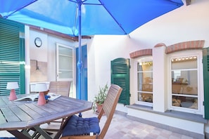 Un patio con una mesa, sillas, una sombrilla azul y una planta en maceta.