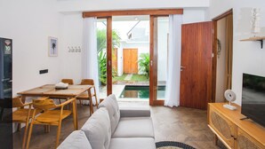 Una sala de estar moderna con sofá, mesa de comedor, sillas, televisor y puerta corrediza de vidrio que da a un jardín.