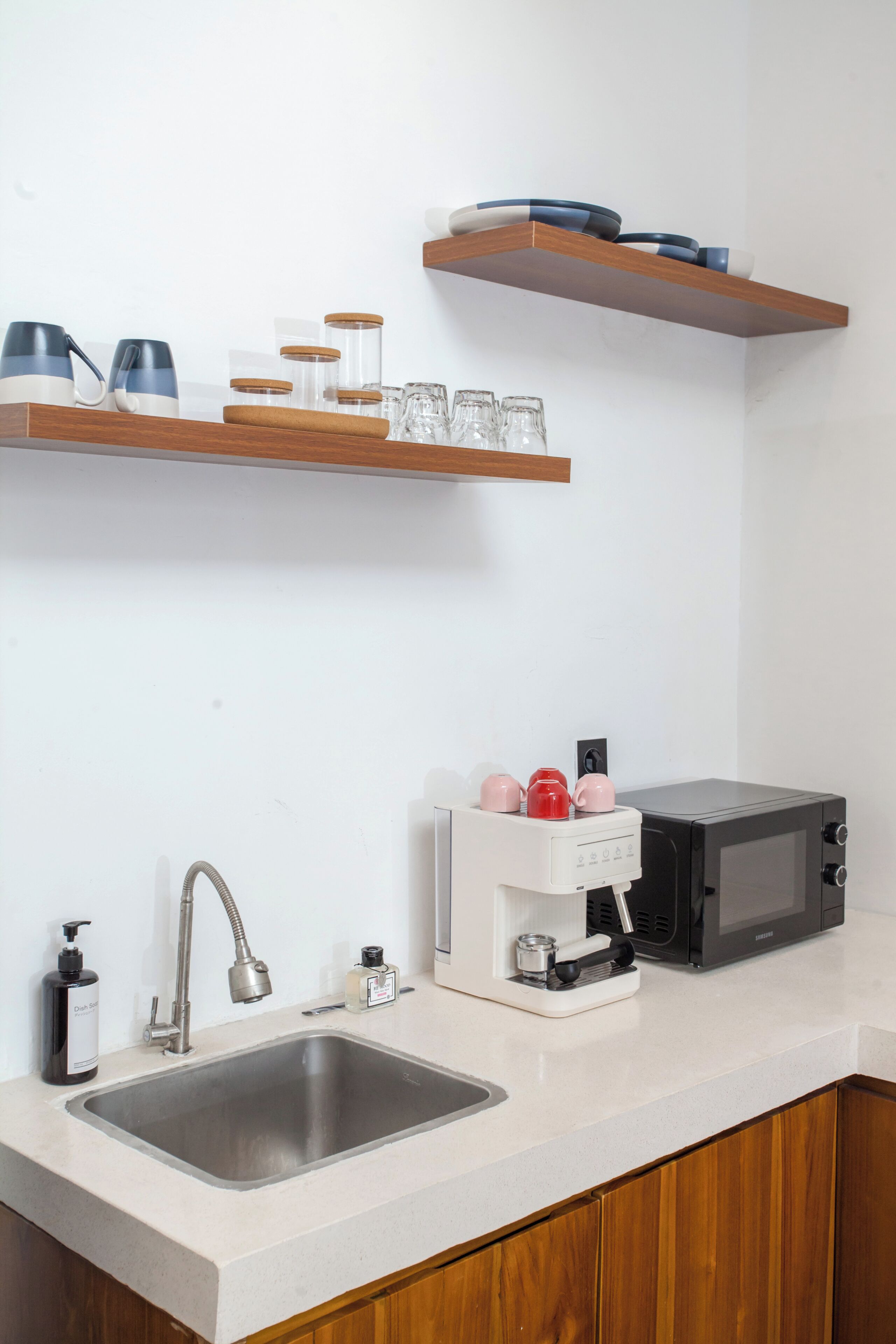 A kitchen with a stainless steel sink, a coffee maker, a microwave, and wooden shelves above the counter.