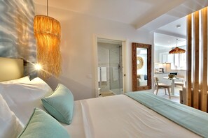 Une chambre d’hôtel avec un lit, un luminaire suspendu, une porte de douche en verre et une vue sur la cuisine.