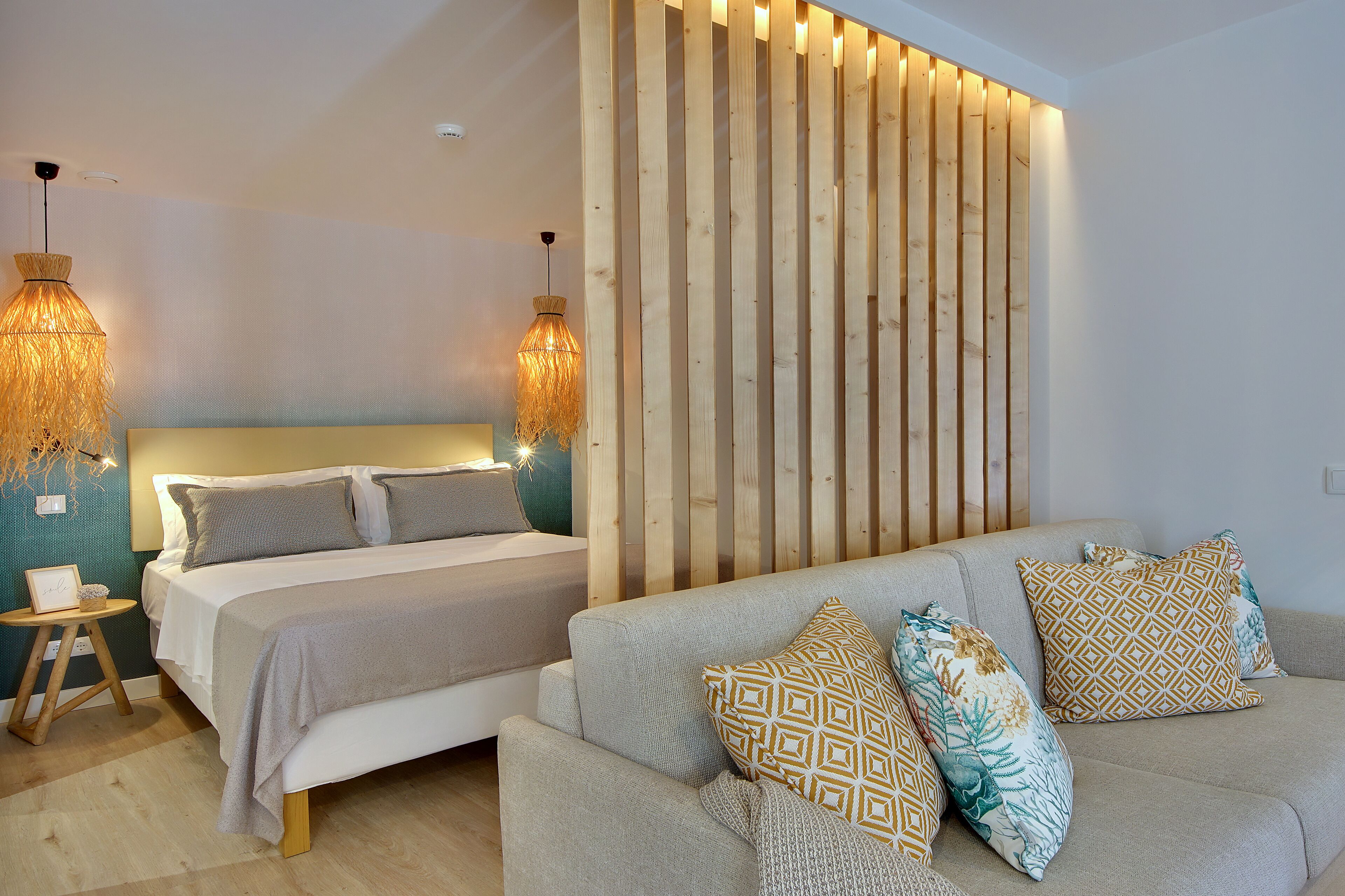 A bedroom with a bed, a sofa, a wooden wall panel, and two hanging lamps.
