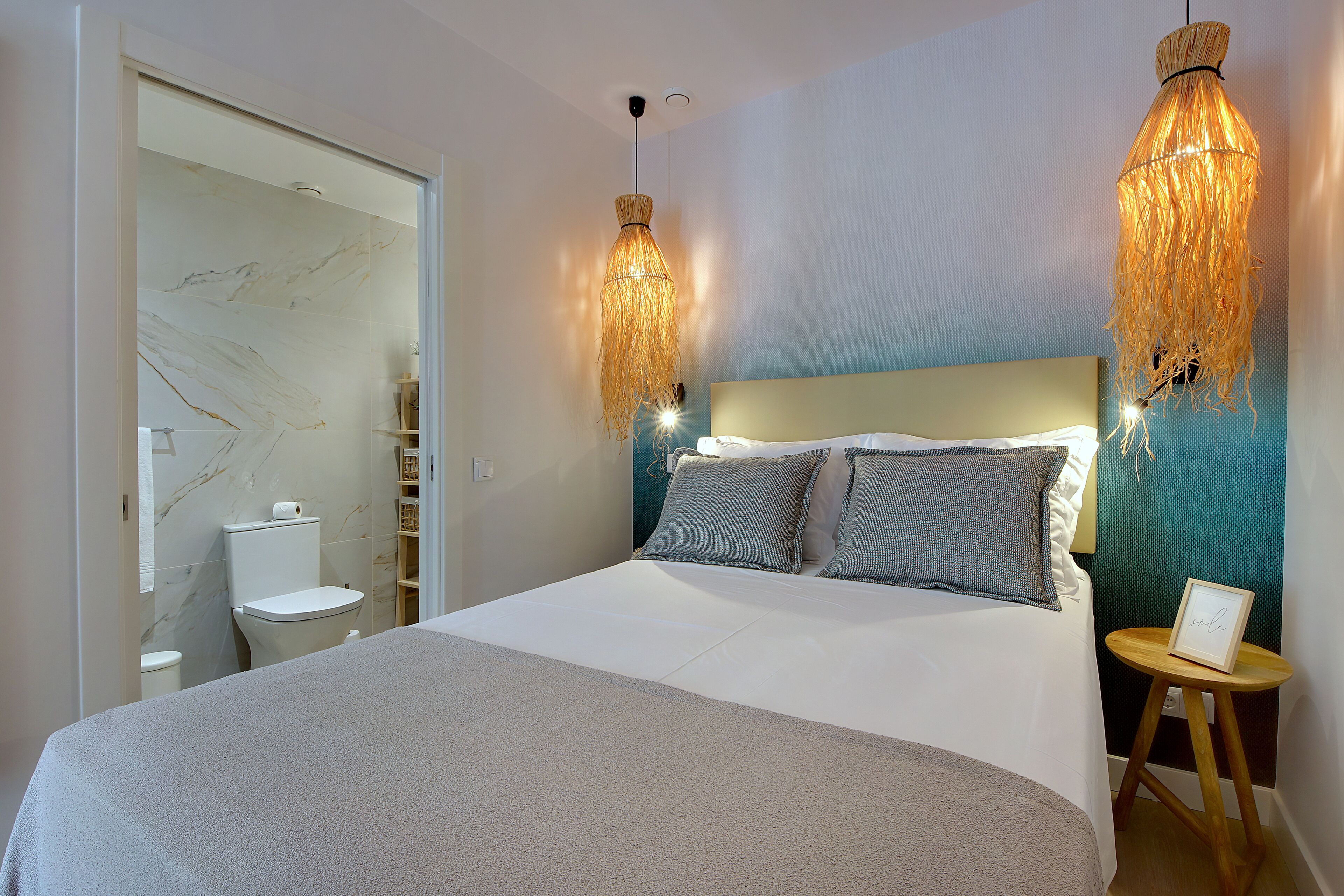 A bedroom with a bed, bedside table, and a hanging light fixture.