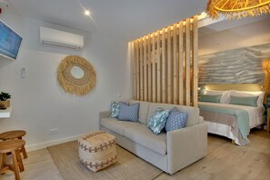 Un soggiorno moderno con un divano, un tavolino di legno, una TV e un letto con testiera.