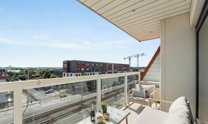 Ein Balkon mit Glasgeländer, der auf Gleise und ein Baugerüst blickt.