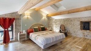 Un dormitorio con cama, vigas de madera, paredes de piedra, una ventana con cortinas y una mesita de noche.