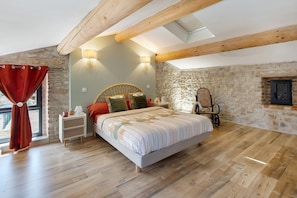 Ein Schlafzimmer mit einem Bett, Holzbalken, Steinwänden, einem Fenster mit Vorhängen und einem Nachttisch.