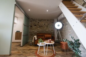 A cozy living room with a stone wall, a wooden staircase, a round table with candles, and a floor lamp.