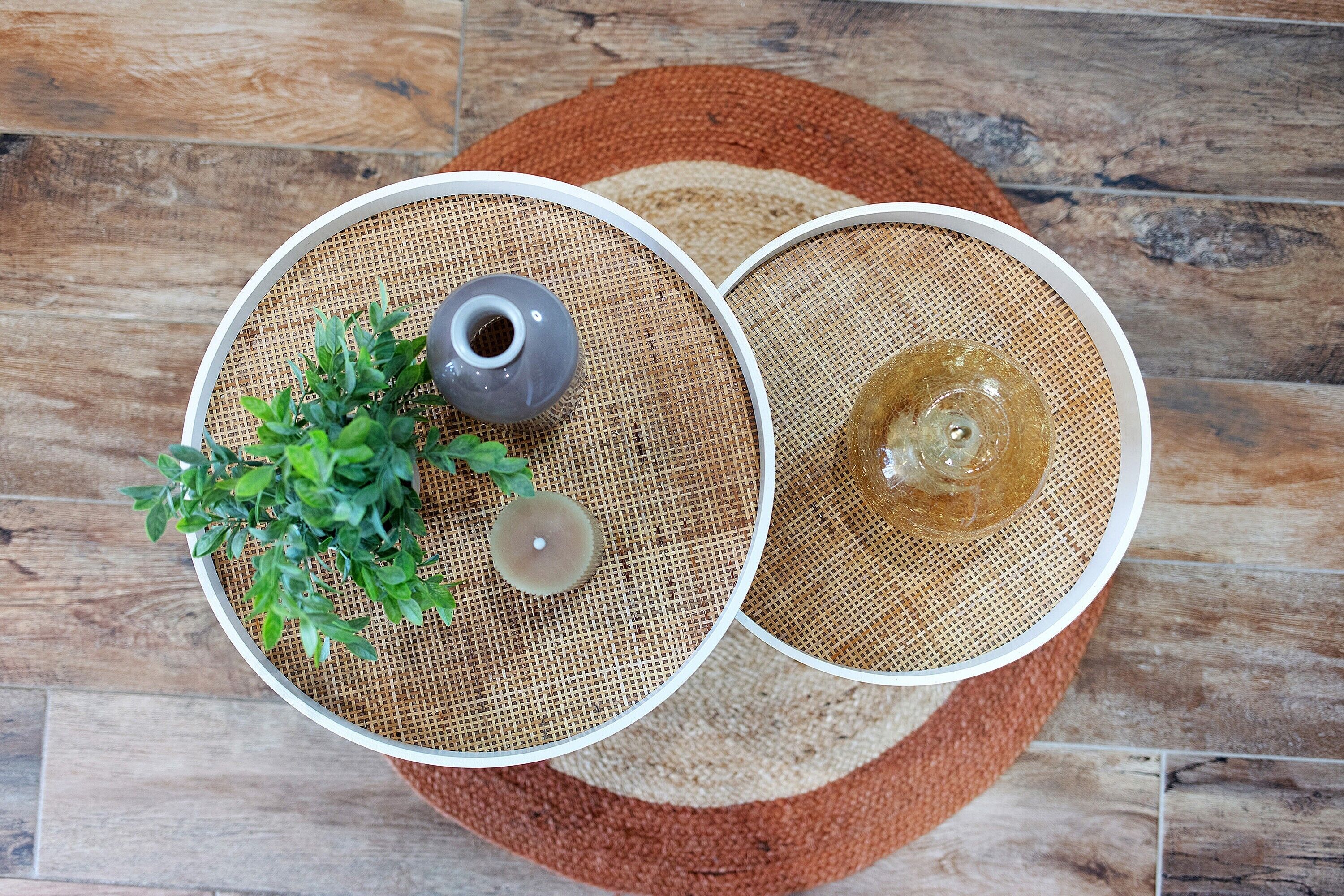 Deux tables rondes surmontées de nattes tissées, l’une avec une plante et un petit récipient, et l’autre avec un objet en verre.