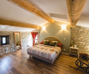 Ein Schlafzimmer mit Bett, Holzbalken, Steinwänden, einem Kamin und einer Steinwand mit Fenster.