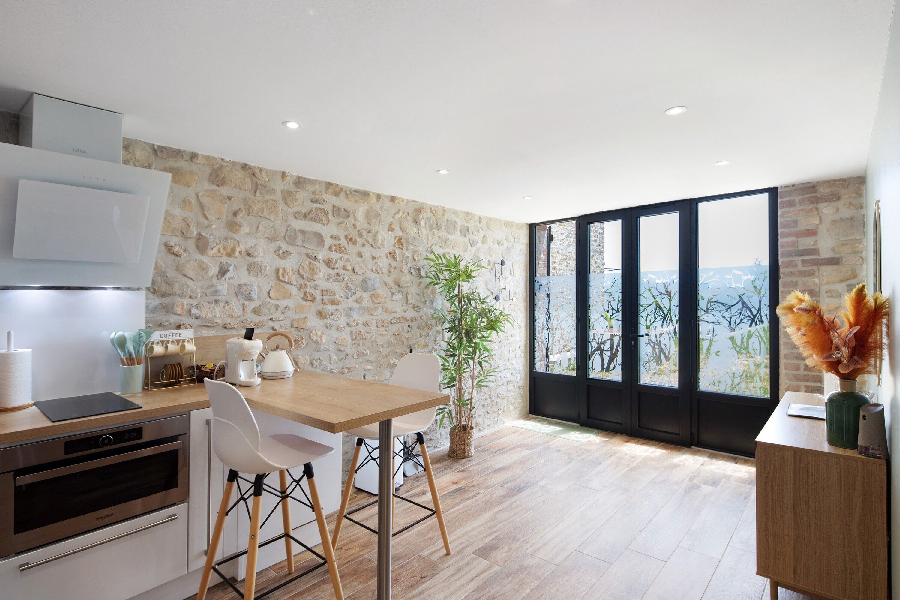 Une cuisine moderne avec un mur en pierre, un coin repas avec une table et des chaises en bois, un espace dédié au café et une grande fenêtre offrant une vue dégagée.