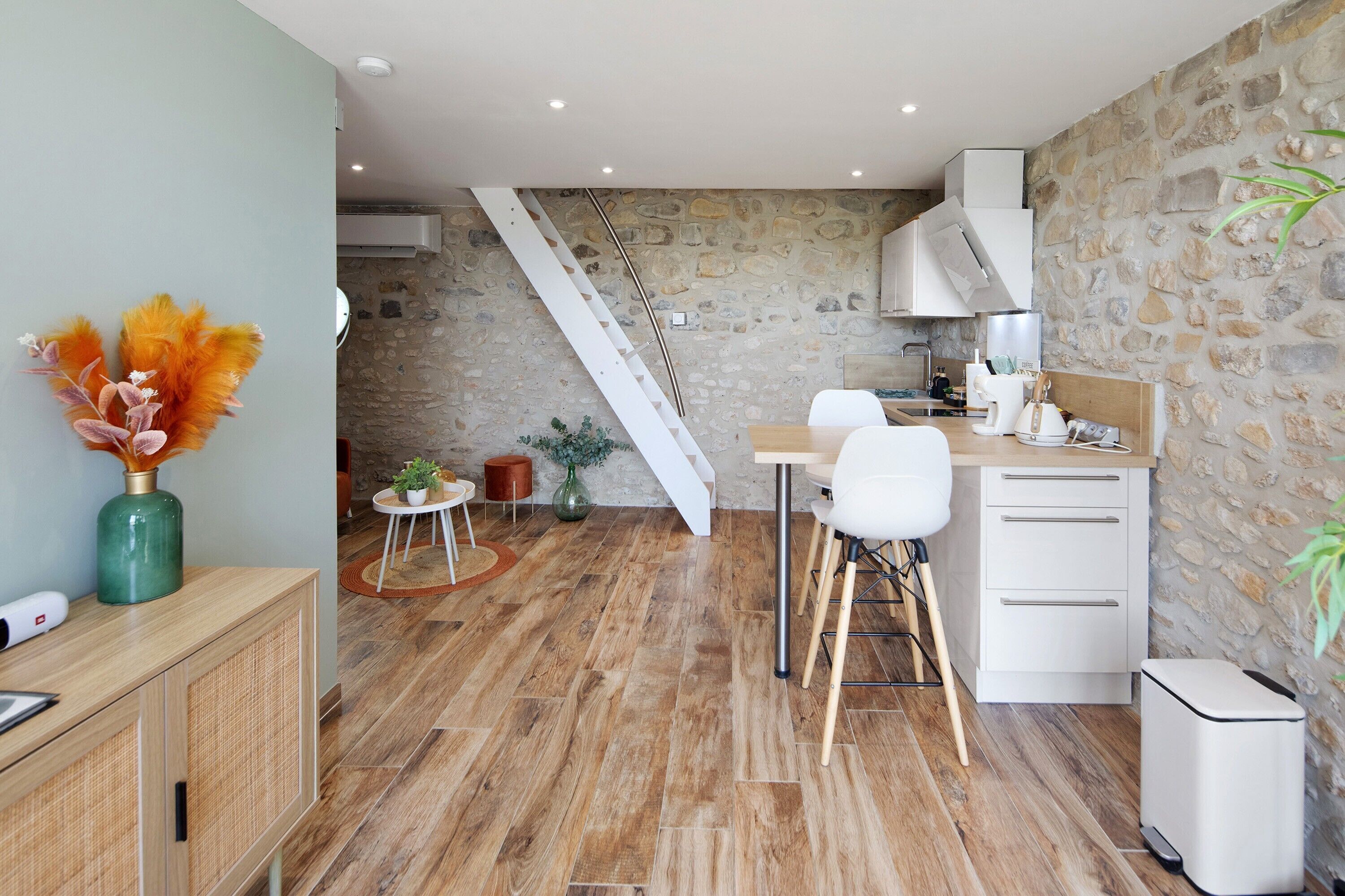 Een moderne keuken met een stenen muur, houten vloeren, een witte trap en een eethoek met witte stoelen en een houten tafel.
