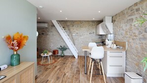 Una cocina moderna con pared de piedra, suelo de madera, una escalera blanca y un comedor con sillas blancas y una mesa de madera.