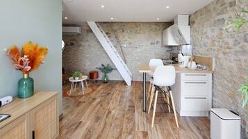 Een moderne keuken met een stenen muur, houten vloeren, een witte trap en een eethoek met witte stoelen en een houten tafel.